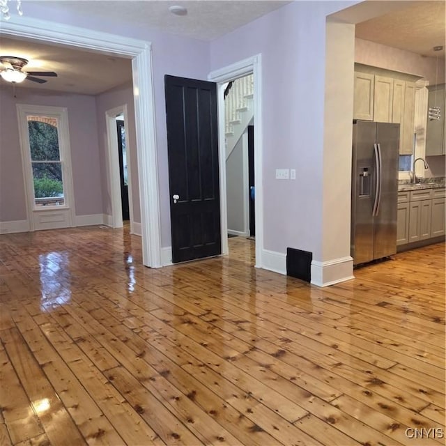 unfurnished living room with light wood-style flooring, a sink, stairway, baseboards, and ceiling fan