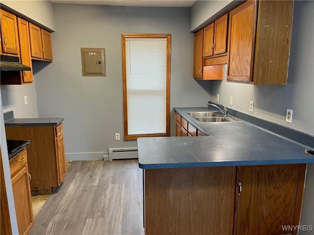 kitchen with a sink, brown cabinets, light wood-style flooring, baseboard heating, and dark countertops