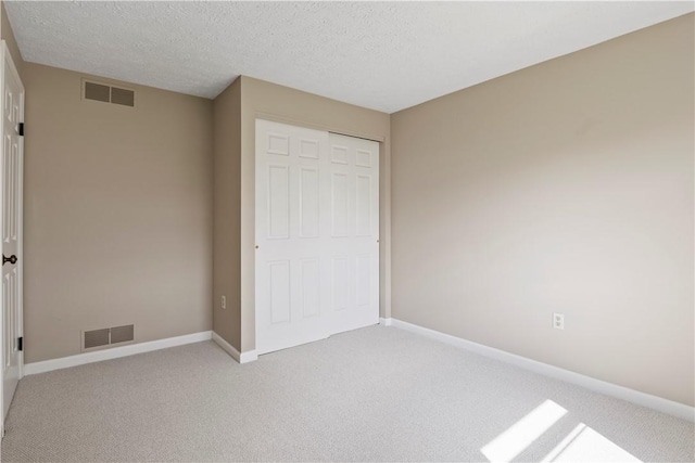 unfurnished bedroom featuring a textured ceiling, visible vents, baseboards, and light carpet