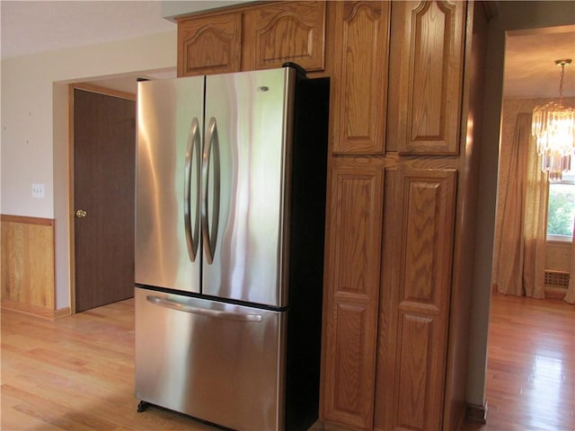 kitchen featuring light wood-style flooring, brown cabinets, freestanding refrigerator, a wainscoted wall, and a chandelier