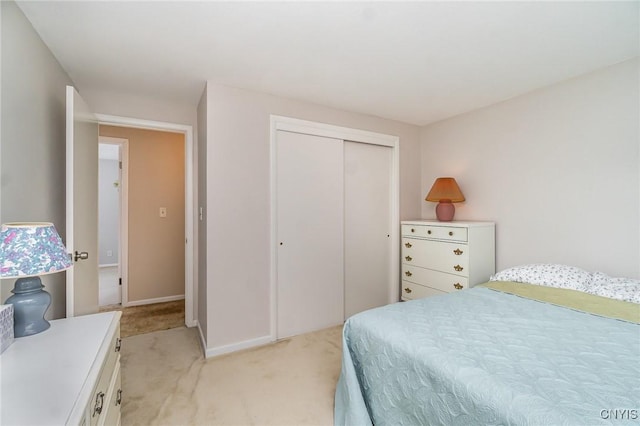 bedroom with a closet, light carpet, and baseboards