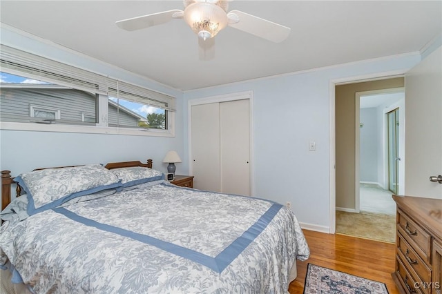 bedroom with a closet, light wood-type flooring, crown molding, a ceiling fan, and baseboards