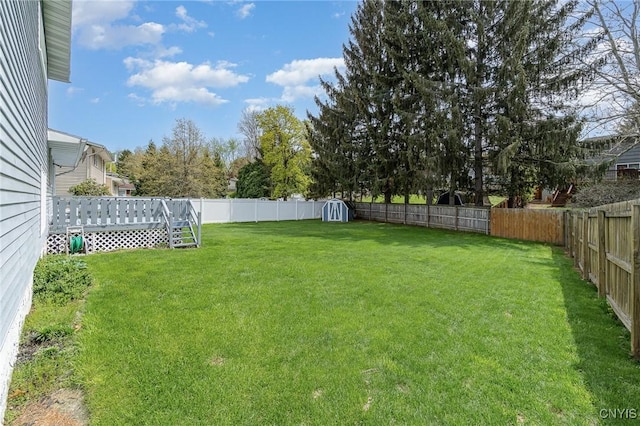 view of yard with an outbuilding, a wooden deck, a storage shed, and a fenced backyard