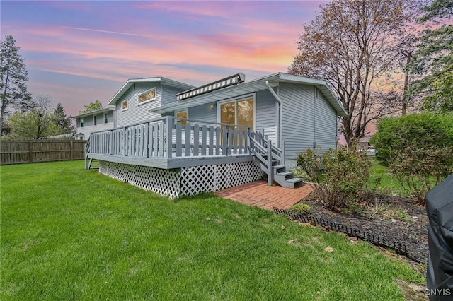 back of house at dusk featuring a yard, fence, and a deck