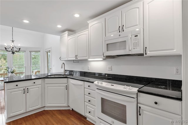 kitchen featuring a peninsula, a sink, a notable chandelier, white cabinets, and white appliances