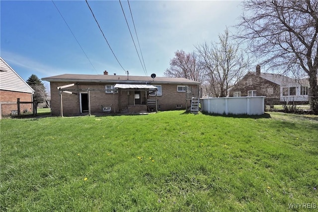rear view of house featuring a yard, brick siding, and an outdoor pool