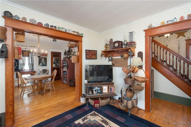 living area with a chandelier, ornamental molding, wood finished floors, and stairway