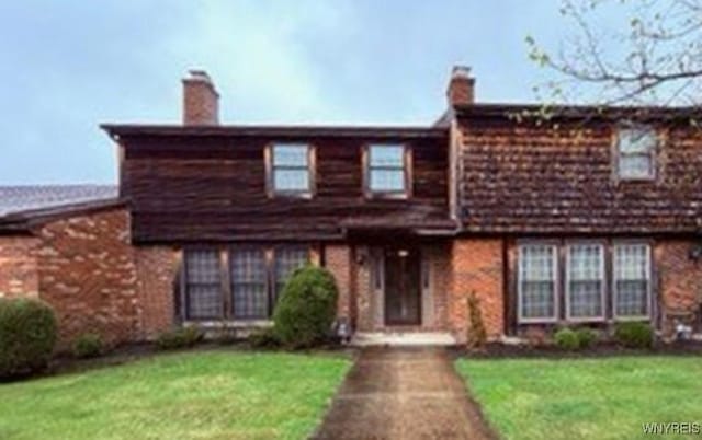view of front facade with a chimney, a front lawn, and brick siding