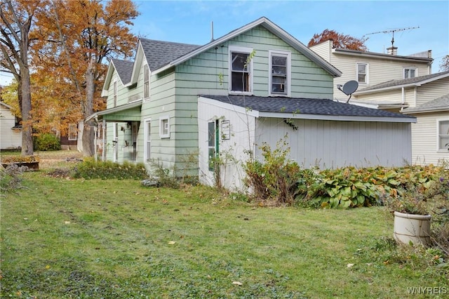 rear view of house featuring a shingled roof and a lawn