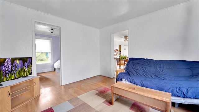 living room with crown molding, light wood-style floors, and a ceiling fan
