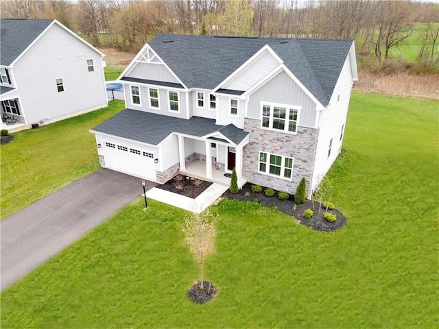 traditional home featuring roof with shingles, aphalt driveway, stone siding, a front lawn, and board and batten siding