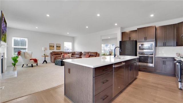kitchen with a sink, open floor plan, light wood-style floors, light countertops, and appliances with stainless steel finishes