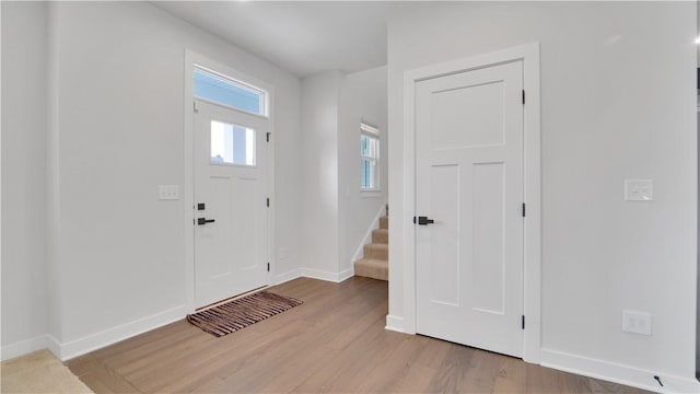 foyer entrance featuring baseboards, stairway, and light wood-style flooring
