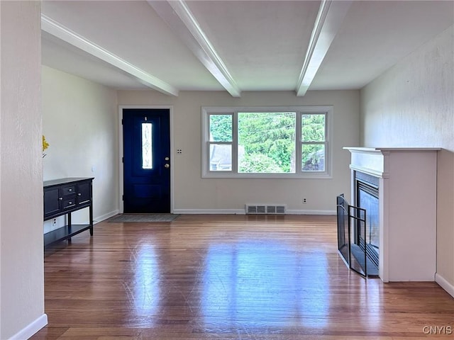 living room featuring wood finished floors, visible vents, baseboards, beamed ceiling, and a glass covered fireplace