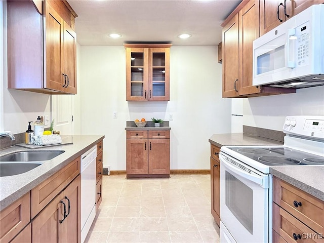 kitchen with a sink, brown cabinetry, white appliances, and glass insert cabinets