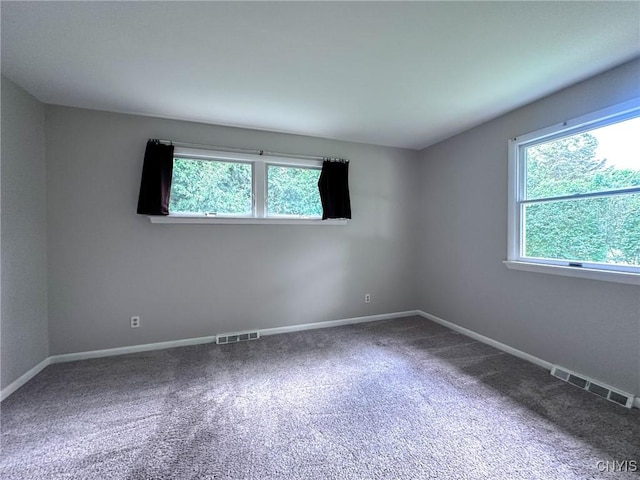 carpeted empty room featuring plenty of natural light, baseboards, and visible vents