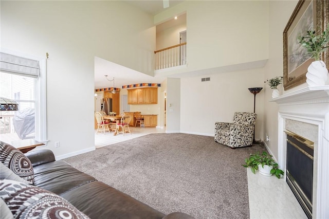 living room with carpet flooring, visible vents, a towering ceiling, and a glass covered fireplace