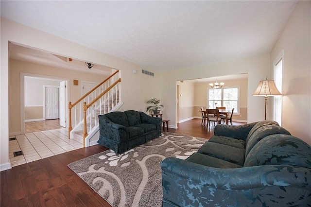 living room with wood finished floors, visible vents, stairway, an inviting chandelier, and baseboards