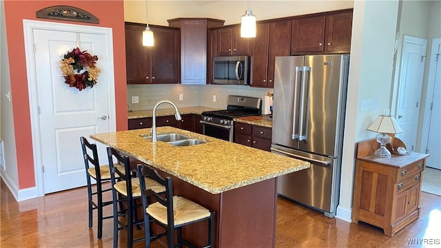 kitchen with a sink, backsplash, hanging light fixtures, baseboards, and appliances with stainless steel finishes
