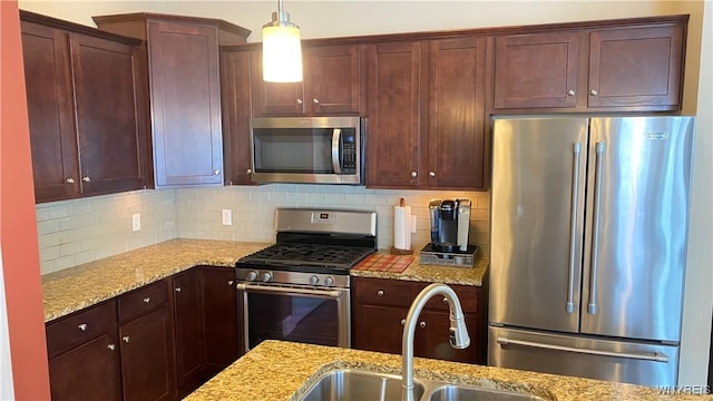 kitchen featuring light stone counters, decorative backsplash, appliances with stainless steel finishes, and a sink