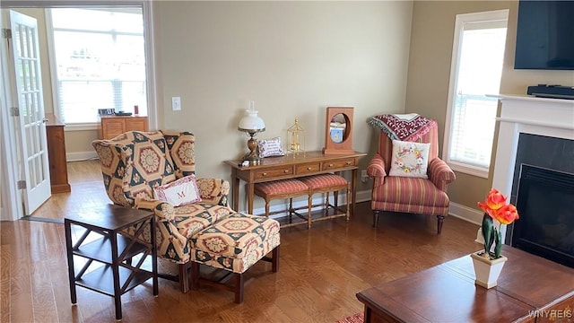 sitting room with baseboards, a healthy amount of sunlight, a glass covered fireplace, and wood finished floors