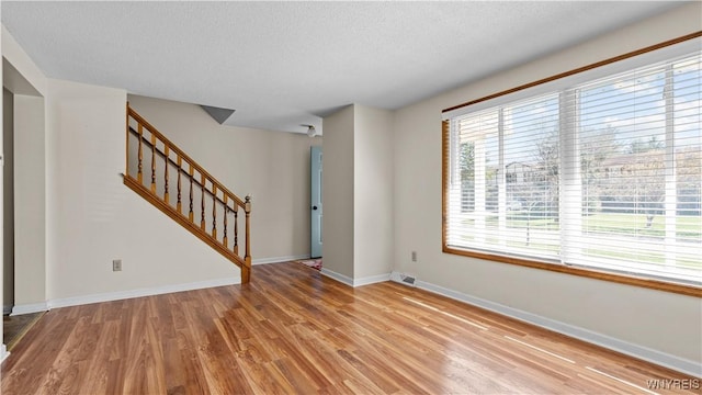 unfurnished living room with stairs, wood finished floors, a textured ceiling, visible vents, and baseboards