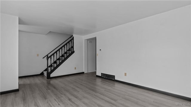 unfurnished living room with visible vents, wood finished floors, baseboards, and stairway