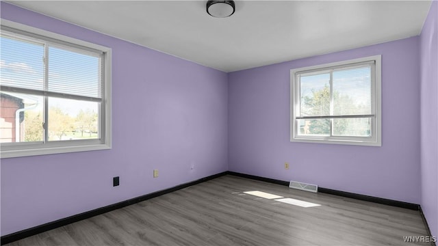 empty room featuring visible vents, wood finished floors, and baseboards