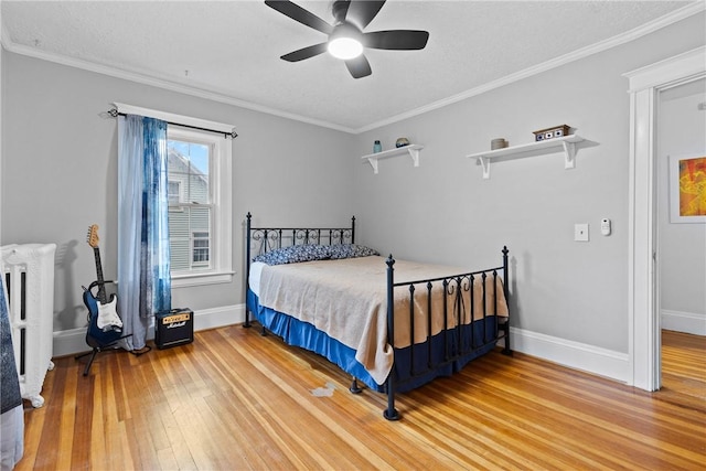 bedroom with a ceiling fan, baseboards, ornamental molding, radiator heating unit, and light wood finished floors