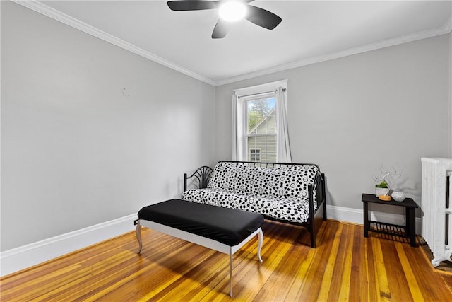 bedroom with radiator heating unit, ornamental molding, wood-type flooring, a ceiling fan, and baseboards