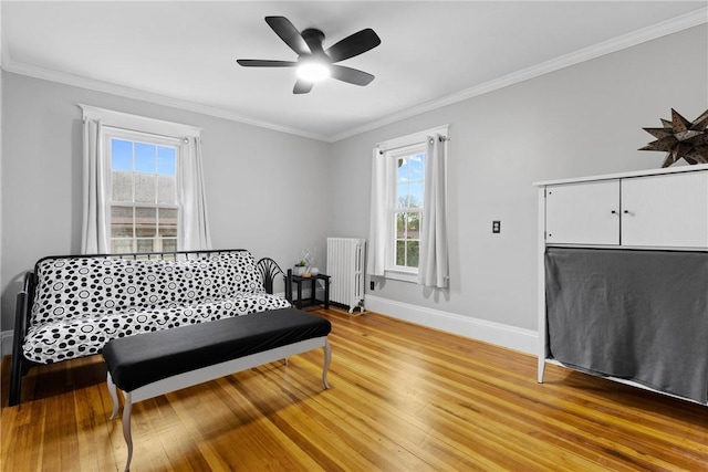 sitting room with a ceiling fan, radiator, baseboards, light wood-style floors, and ornamental molding