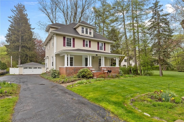american foursquare style home featuring covered porch, an outbuilding, a front lawn, and a detached garage