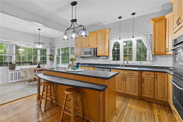 kitchen with a sink, light wood-style flooring, dark countertops, and appliances with stainless steel finishes