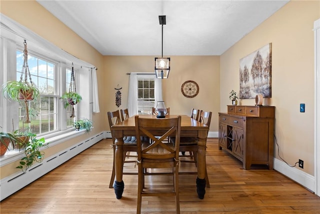 dining area with a baseboard heating unit, baseboards, and light wood-type flooring