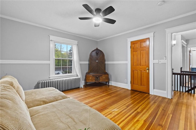 living area with baseboards, radiator, ceiling fan, wood-type flooring, and crown molding