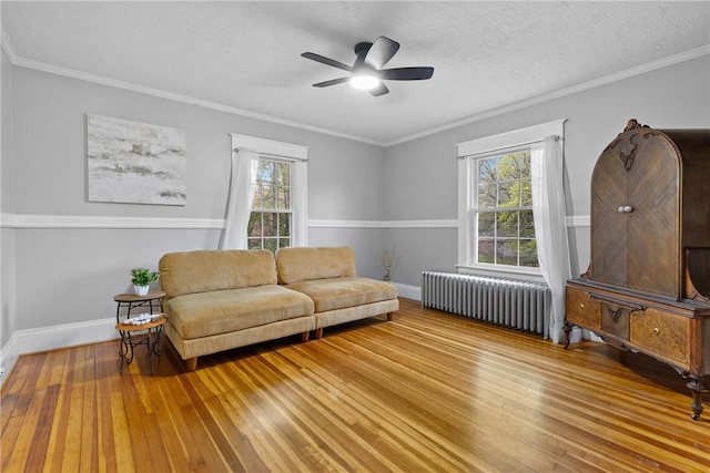 living room with hardwood / wood-style flooring, radiator, crown molding, a ceiling fan, and baseboards