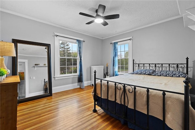 bedroom featuring a textured ceiling, baseboards, radiator, ceiling fan, and light wood-type flooring