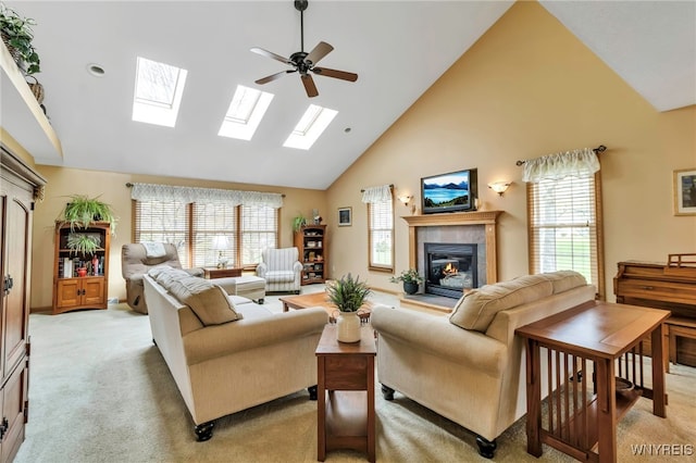 living room featuring high vaulted ceiling, a fireplace, a skylight, ceiling fan, and light colored carpet