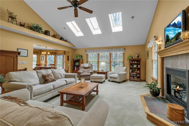 living area with ceiling fan with notable chandelier, high vaulted ceiling, a fireplace, a skylight, and light carpet