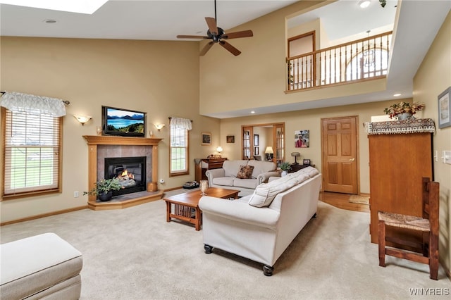 living room featuring light colored carpet, high vaulted ceiling, ceiling fan, baseboards, and a tile fireplace