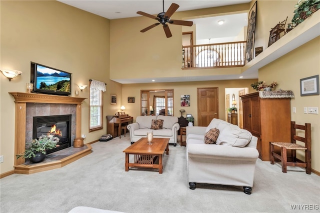 living area with a fireplace, ceiling fan, a towering ceiling, and carpet