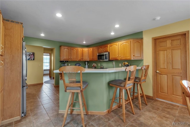 kitchen featuring a kitchen breakfast bar, recessed lighting, light countertops, baseboards, and appliances with stainless steel finishes