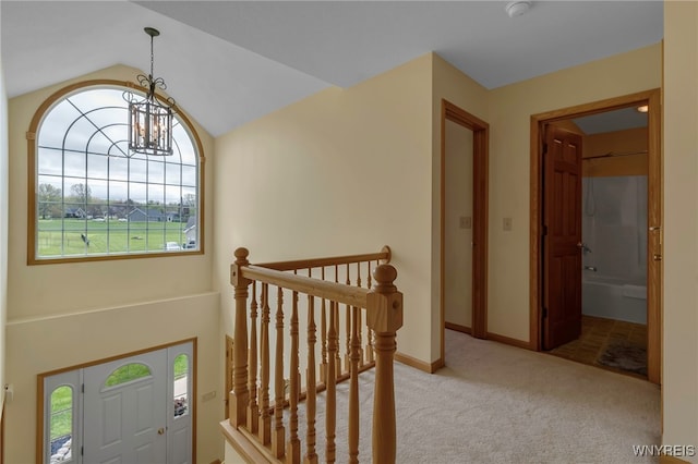 carpeted foyer entrance with baseboards, a wealth of natural light, a notable chandelier, and vaulted ceiling