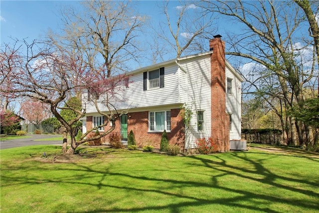 colonial home with a chimney, brick siding, cooling unit, a front yard, and aphalt driveway