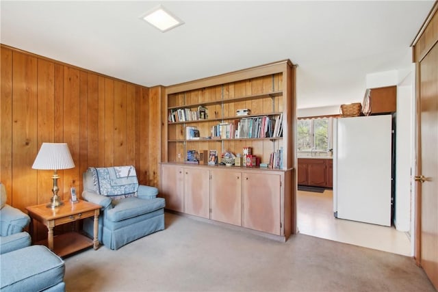 sitting room featuring wooden walls and light carpet