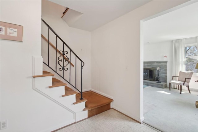 staircase with carpet flooring, baseboards, and a glass covered fireplace