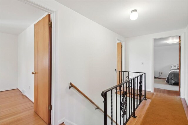 corridor with baseboards, an upstairs landing, and light wood-style floors
