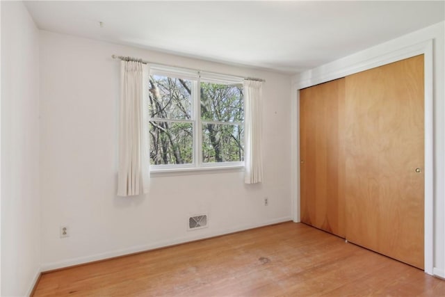 unfurnished bedroom featuring a closet, baseboards, visible vents, and wood finished floors