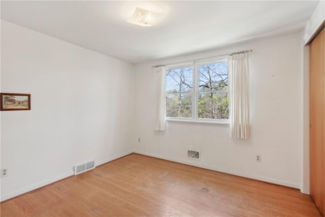 unfurnished room featuring baseboards, light wood-type flooring, and visible vents