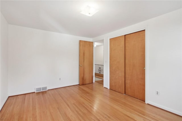 unfurnished bedroom featuring baseboards, light wood-style floors, a closet, and visible vents